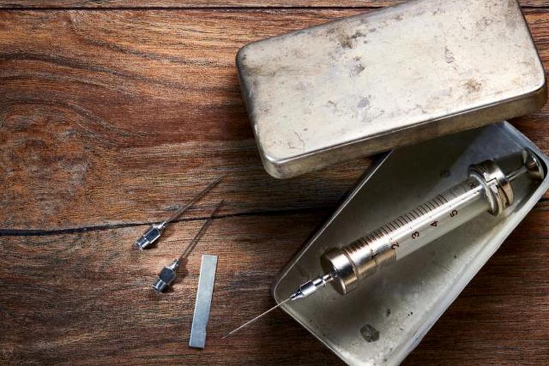 Винтажный стеклянный шприц в металлической коробке и иглы на деревянном столе