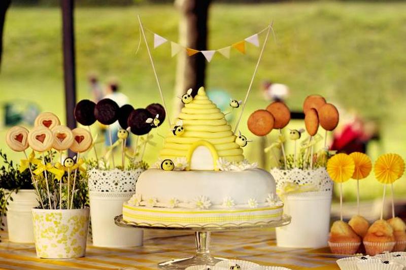 Конфеты, печенье, кексы и торт в виде сот с летающими помадными пчелами и милыми желтыми флажками.