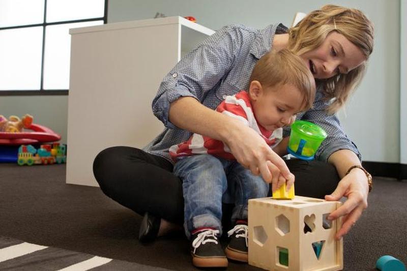 Няня и мальчик играют с геометрической коробкой-головоломкой 