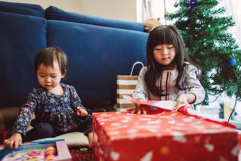 милая маленькая девочка открывает рождественские подарки со своей младшей сестрой дома