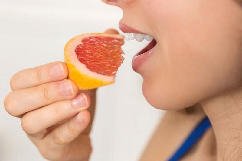 Женщина ест кусочек грейпфрута