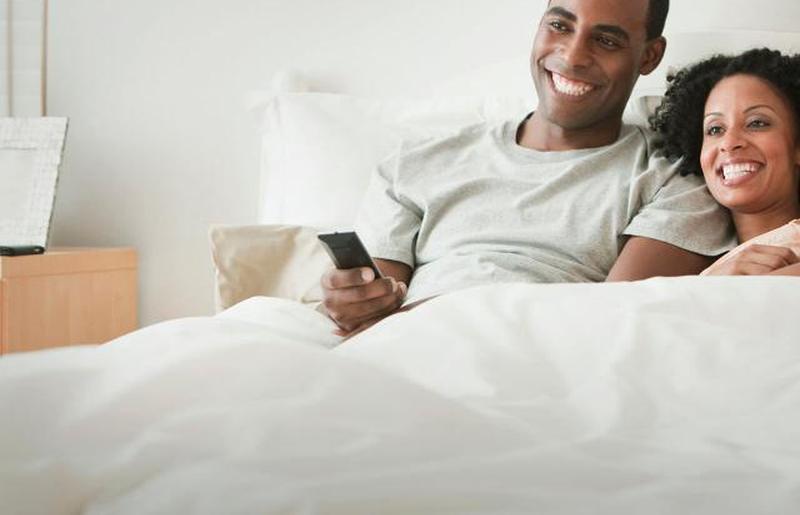 Пара лежит в постели и смотрит телевизор