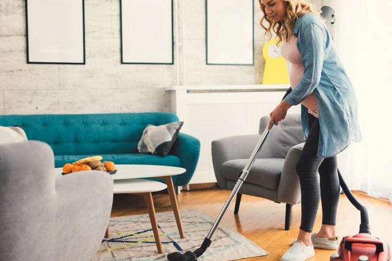 Беременная женщина пылесосит ковер 