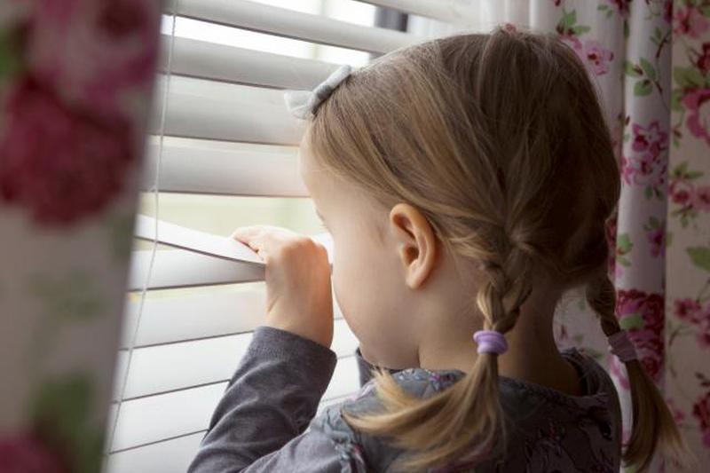 Ребенок в помещении выглядывает через жалюзи