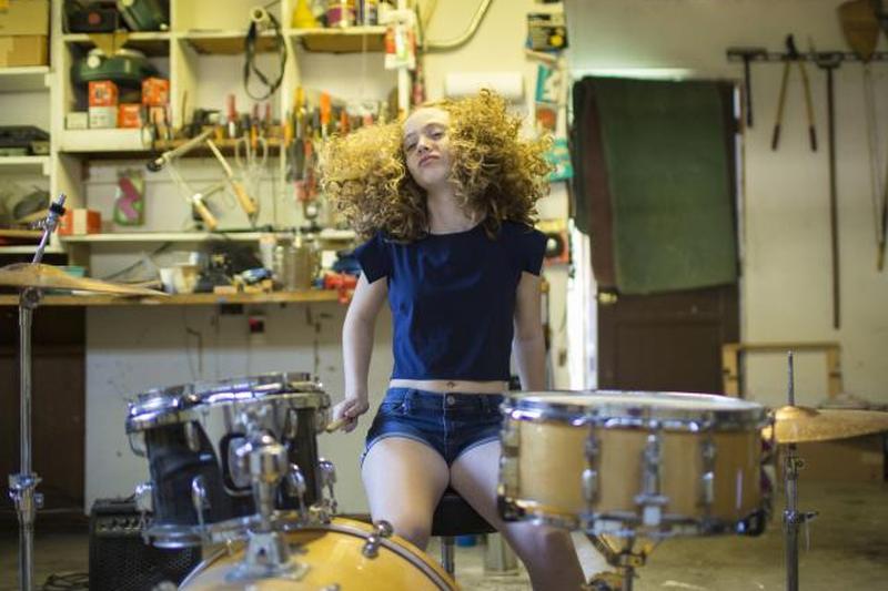 Девочка-подросток играет на барабанах в гараже