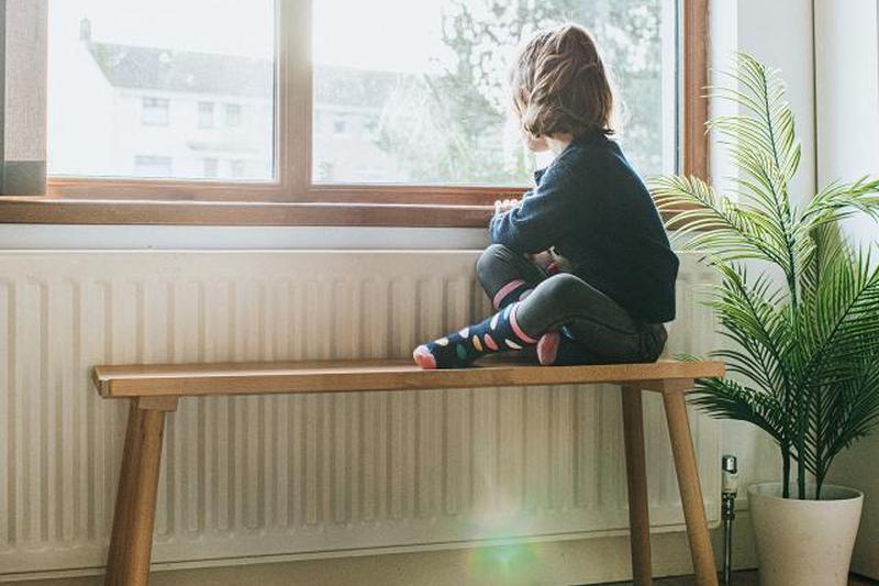 Маленькая девочка сидит на скамейке у солнечного окна