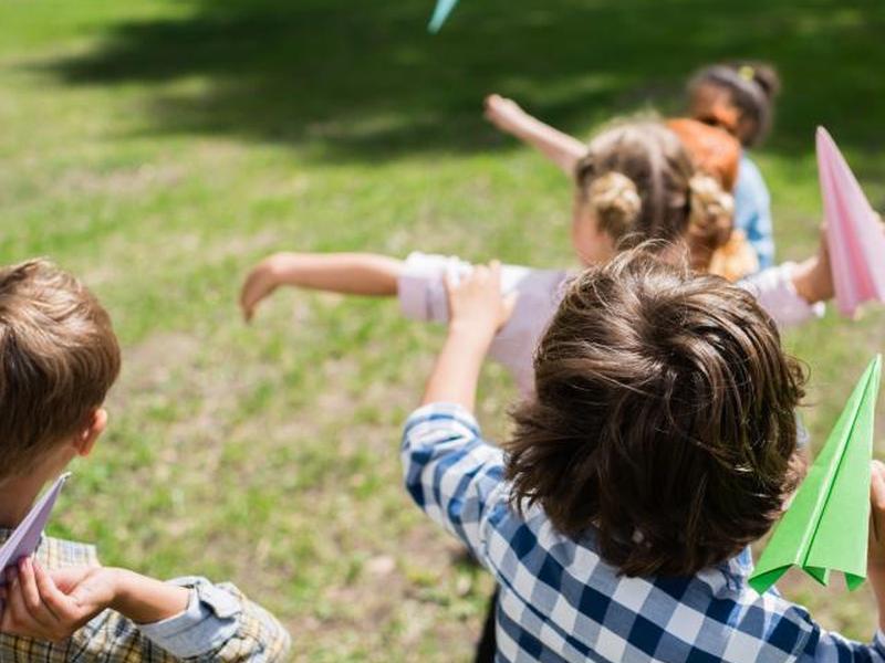 Маленькие дети бросают бумажные самолетики на улицу