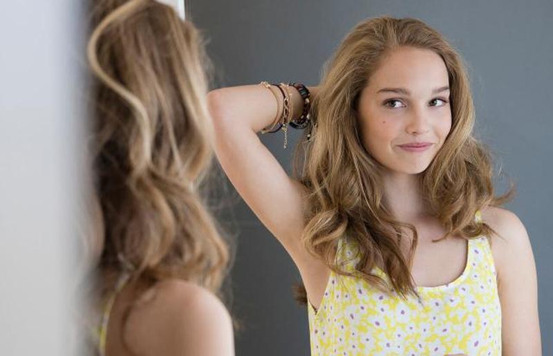 Девочка-подросток рассматривает свои волосы в зеркале