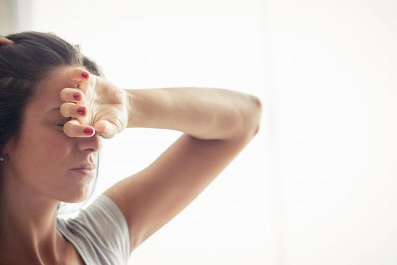 Молодая женщина держит одну руку на лбу