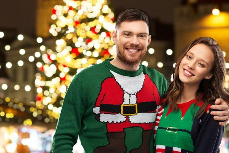 счастливая пара в уродливых свитерах на рождественской ярмарке 
