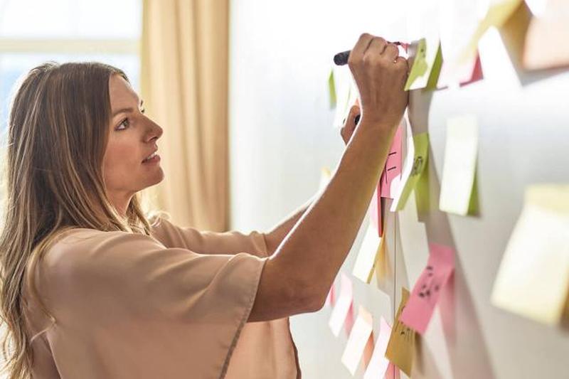 Женщина пишет на заметке у стены 