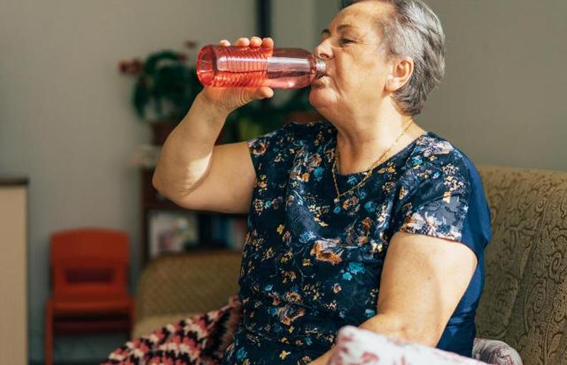 Пожилая женщина пьет из бутылки с водой