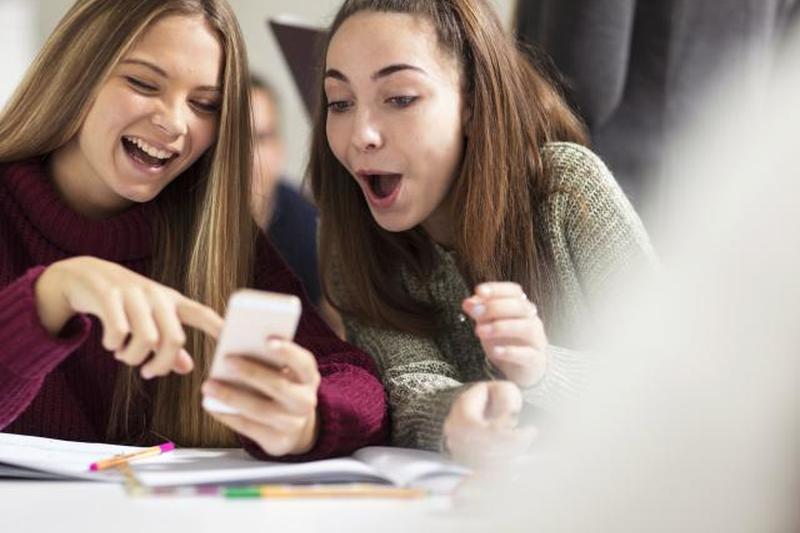 Девочки-подростки в классе смотрят на мобильный телефон