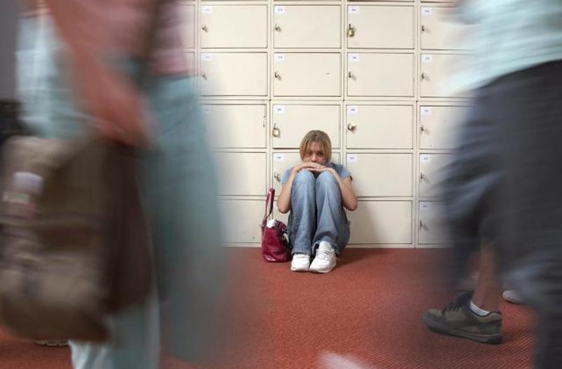 Девочка-подросток сидит у шкафчиков в школьном коридоре
